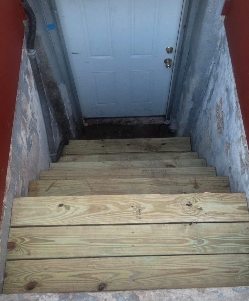 After: New pressure-treated wood steps in the same bulkhead stairwell, leading to the basement door