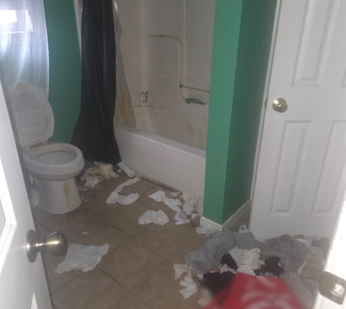 Before: Rental unit bathroom left trashed, with clothing and debris across the floor