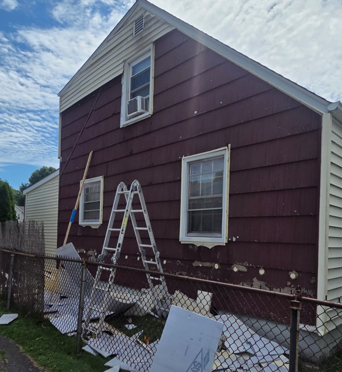 Before: Exterior of a two-story house with worn red siding being torn off, debris and a ladder against the wall